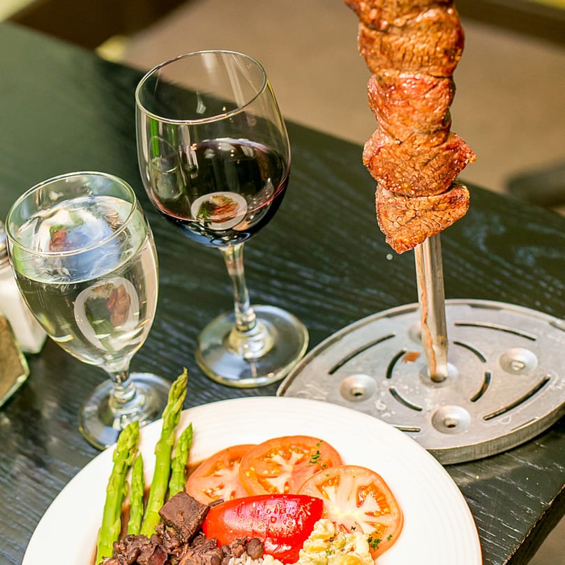 Brazilian picanha steak on a skewer, with a side of black beans, rice, tomatoes, and asparagus.